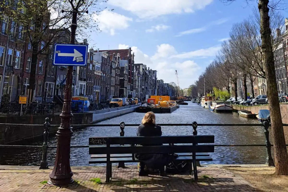 Person sits on bench next to Amsterdam's canal